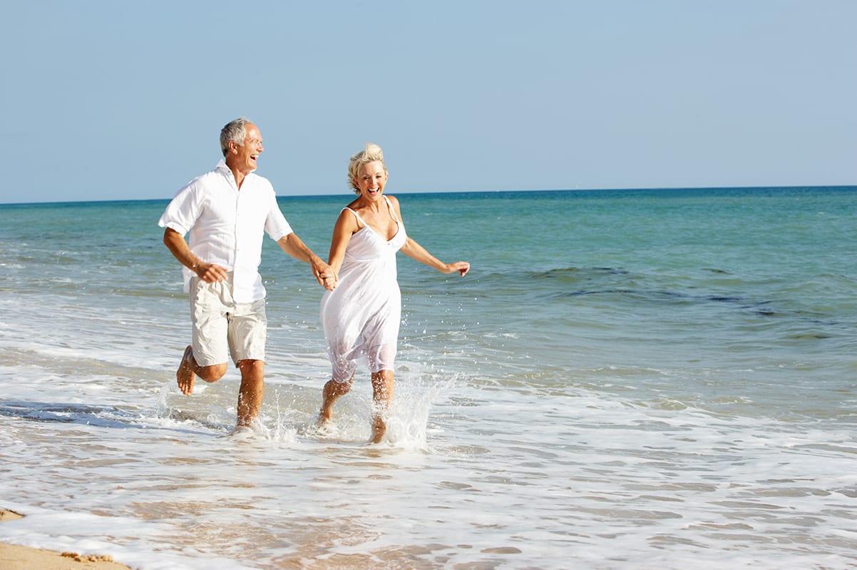 Older couple running on the beach enjoying their retirement